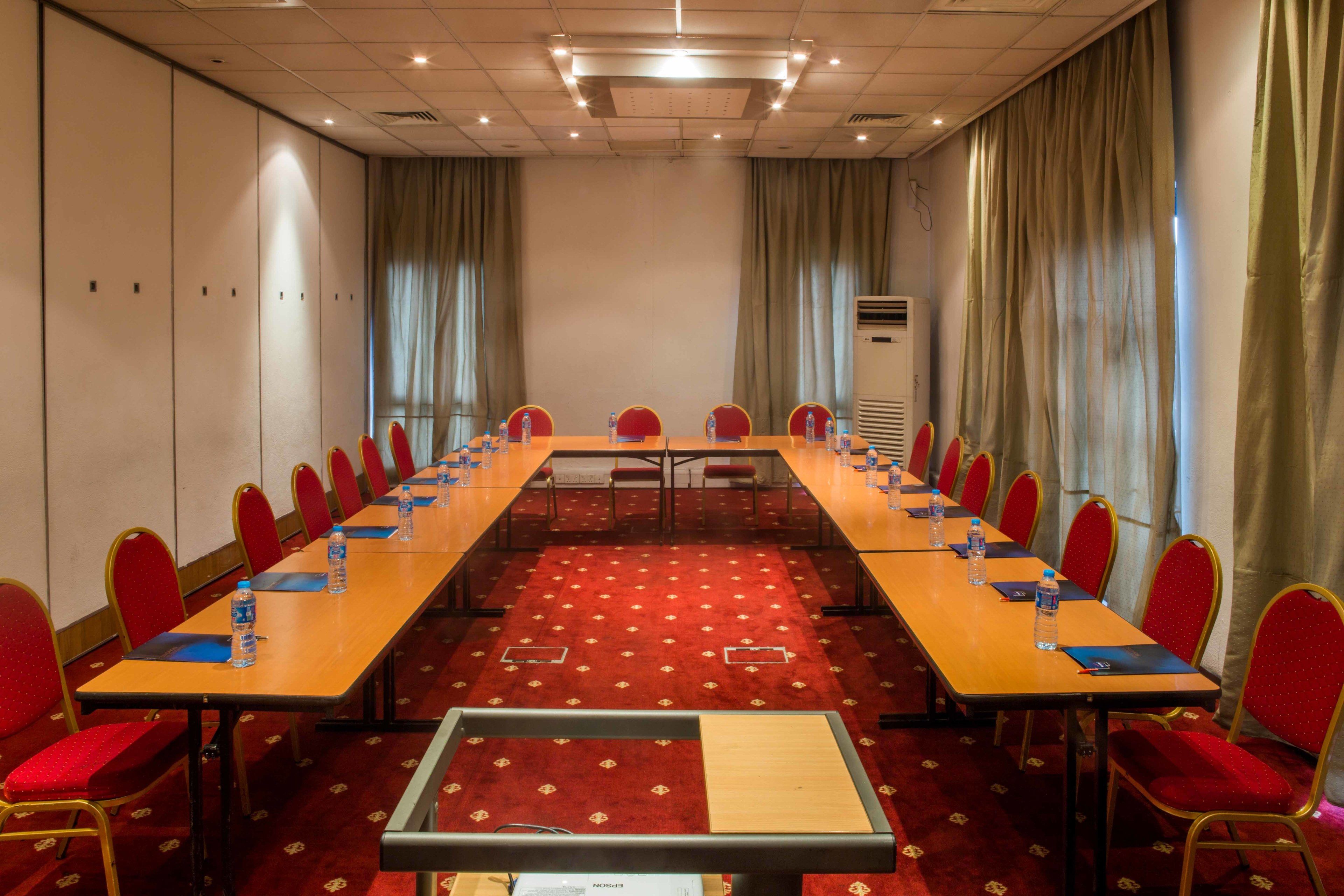 A conference room with a long table, red chairs, and a carpeted floor.