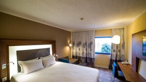 A hotel room with a large bed, a desk, a chair, a window with curtains, and a ceiling light. - Novotel Port Harcourt (Port Harcourt)