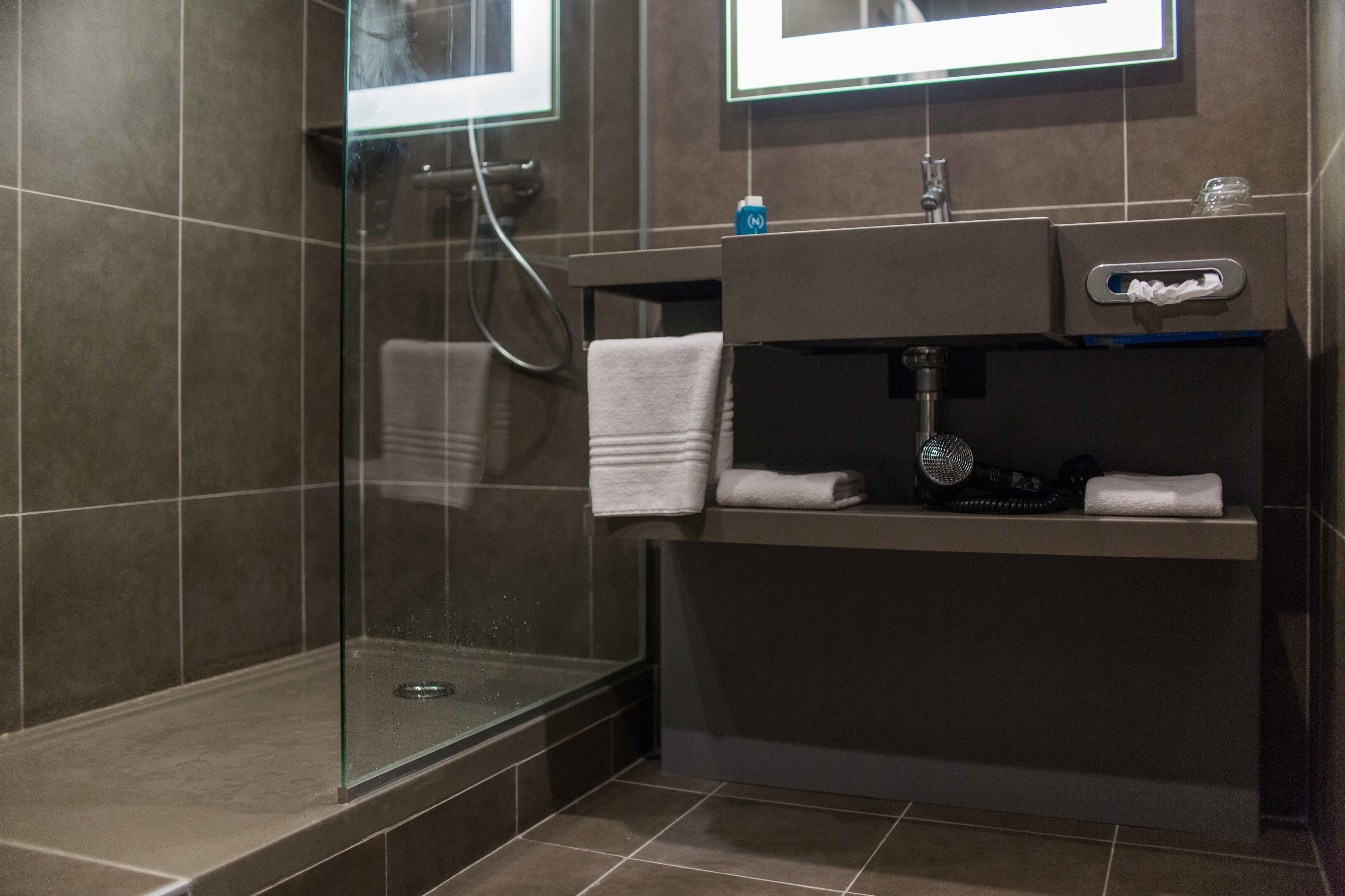 A modern bathroom with a glass-enclosed shower, a vanity with a mirror, and a towel rack.
