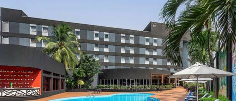 A hotel with a swimming pool, lounge chairs, and palm trees.
