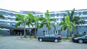 A modern hotel with a checkered facade, palm trees in front, and a black car parked in the driveway.