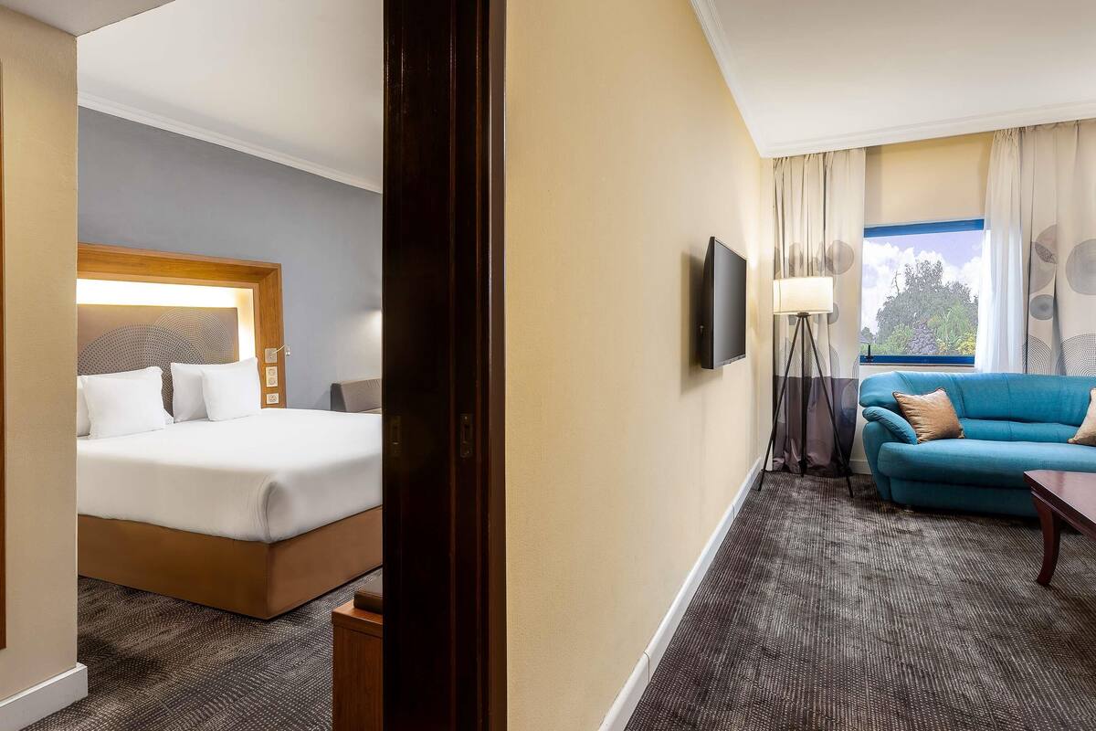 A hotel room with a bed, a sofa, a TV, and a window with curtains.