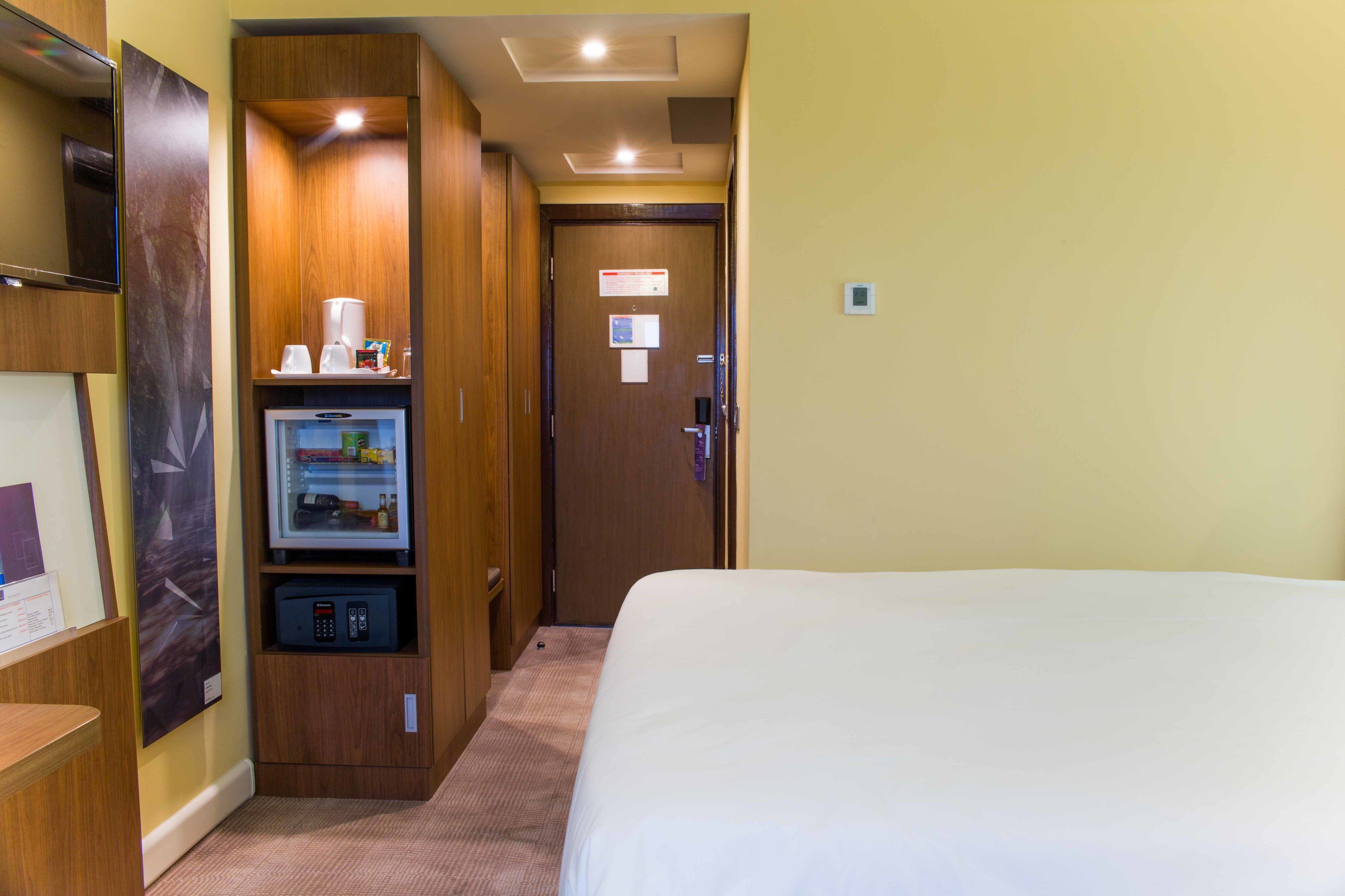 A hotel room with a bed, a minibar, a television, and a wooden wardrobe.