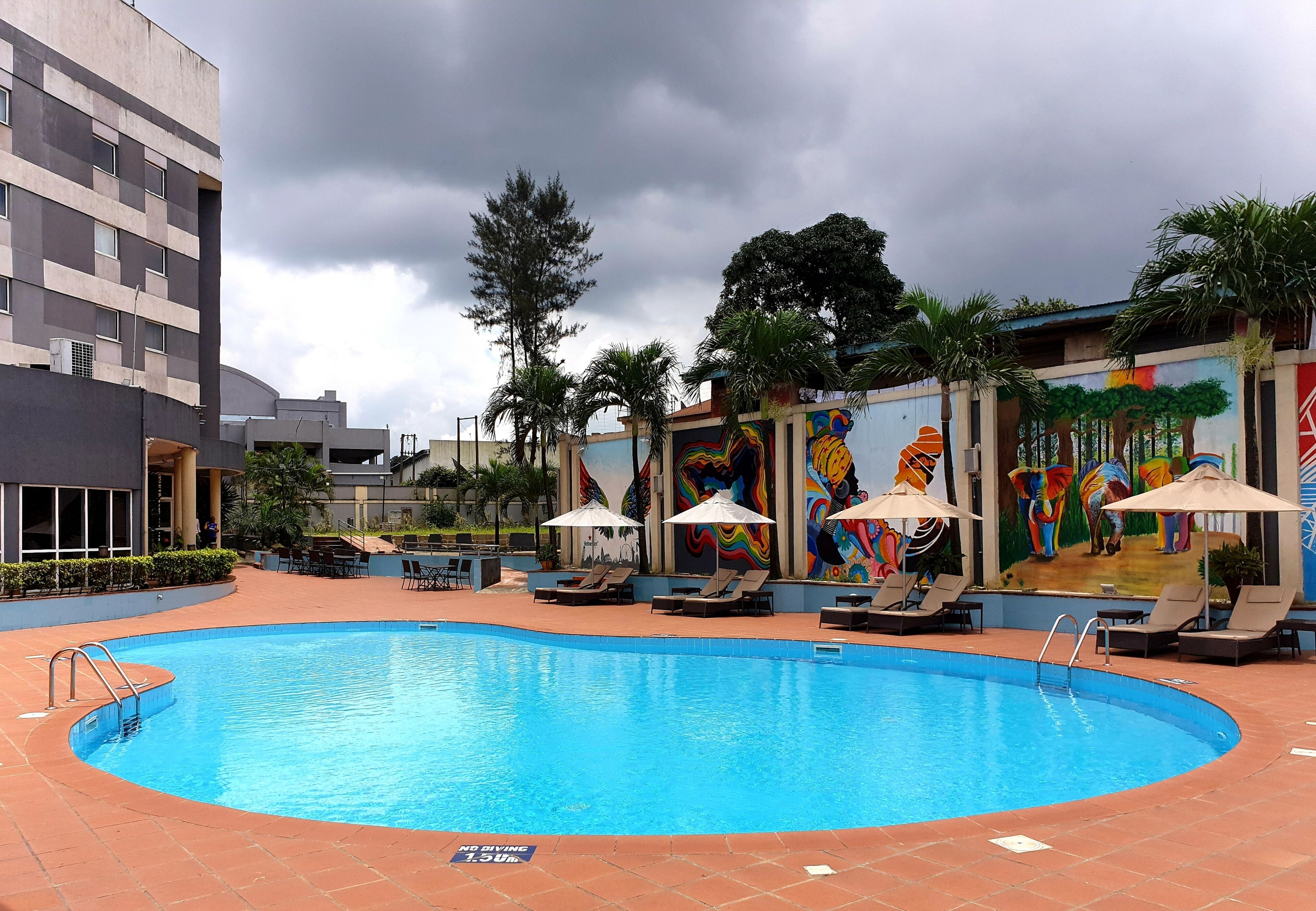 A swimming pool with lounge chairs and umbrellas, surrounded by a building with a mural.