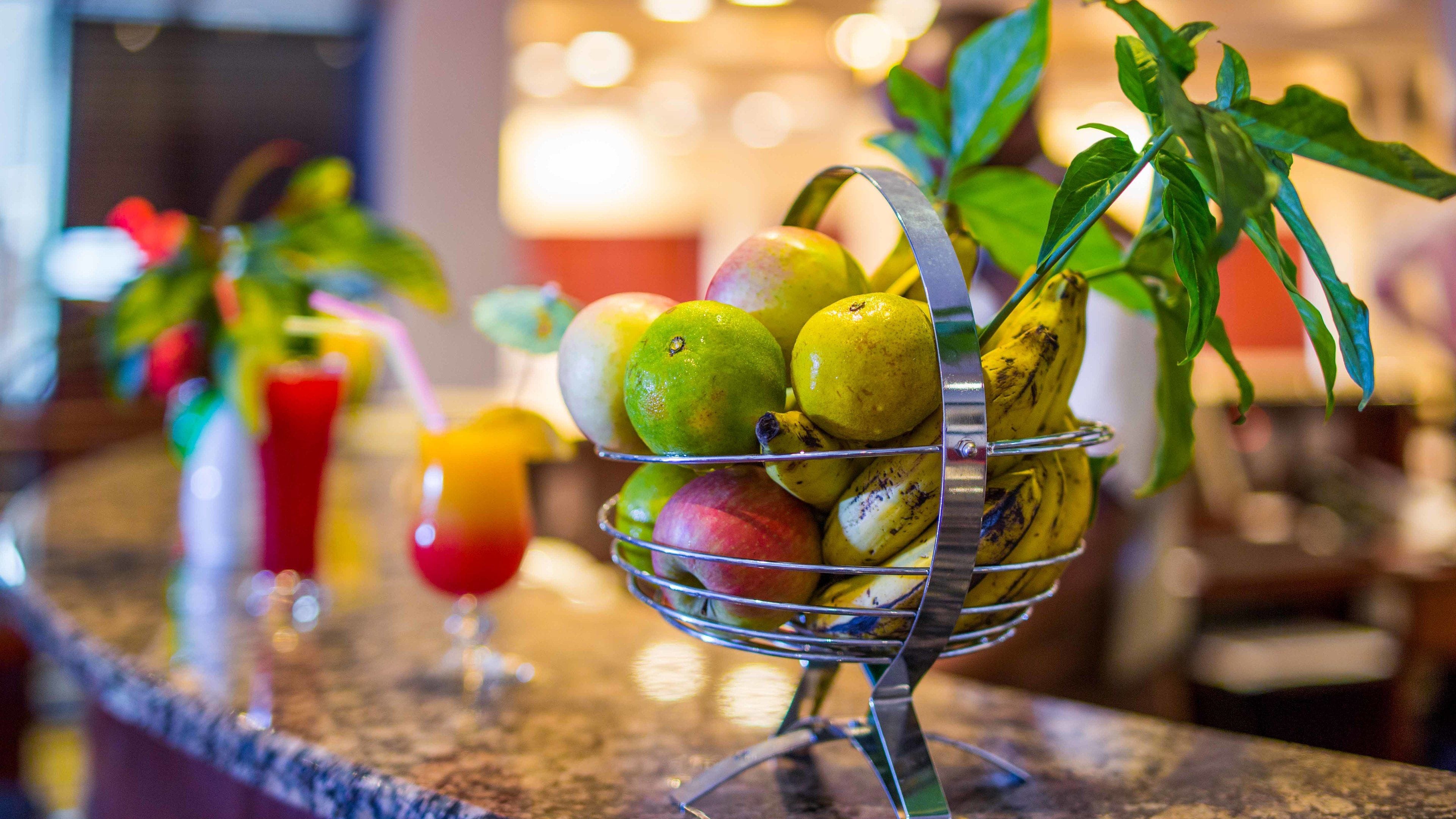 A fruit basket on a bar counter with various fruits and a banana plant.