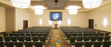 A conference room with rows of chairs, a carpeted floor, and a large screen at the front.