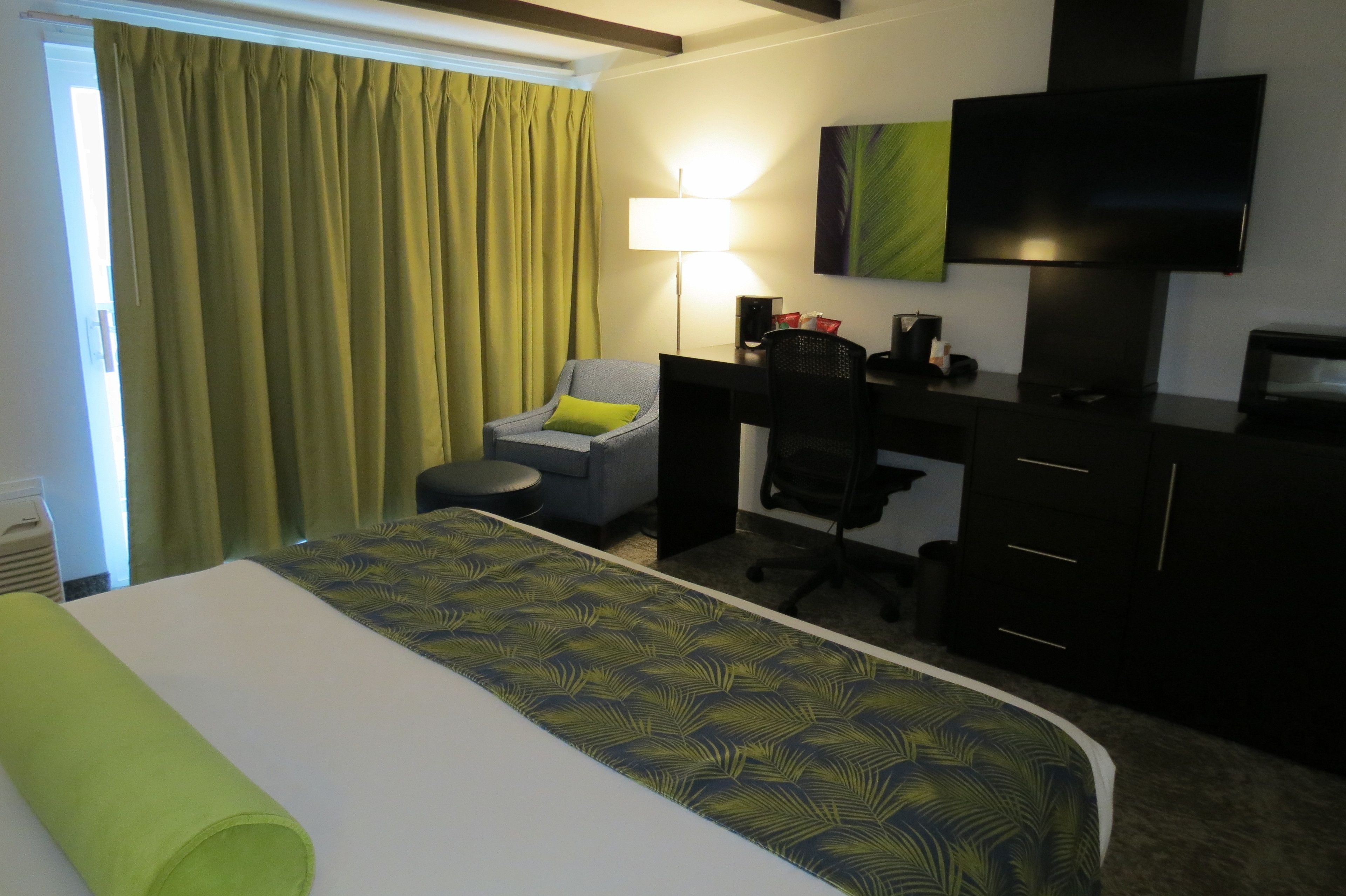 Una habitación de hotel con una cama, un escritorio, una silla, un televisor y una lámpara.