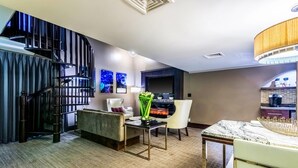 A modern hotel room with a spiral staircase, a fireplace, a dining area with a marble table, and a seating area with a sofa and armchairs. - Oasis Hotel & Conv. Center, an Ascend Collection Hotel (Springfield)