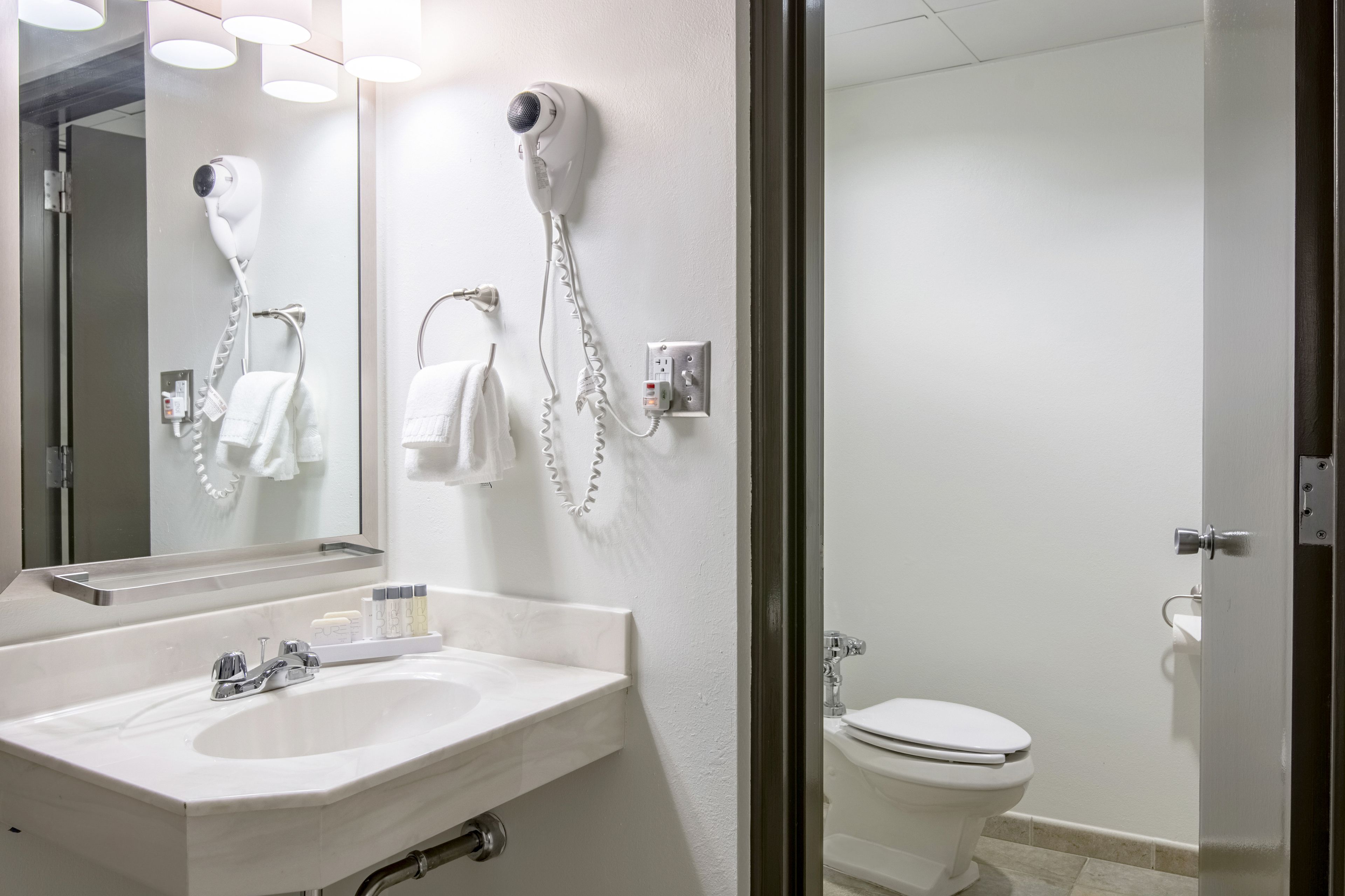 Un baño moderno con un lavamanos blanco, un secador de pelo montado en la pared y un inodoro.