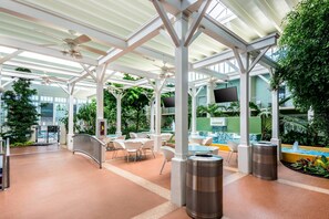 An indoor atrium with a glass ceiling, white columns, and a central seating area with tables and chairs.