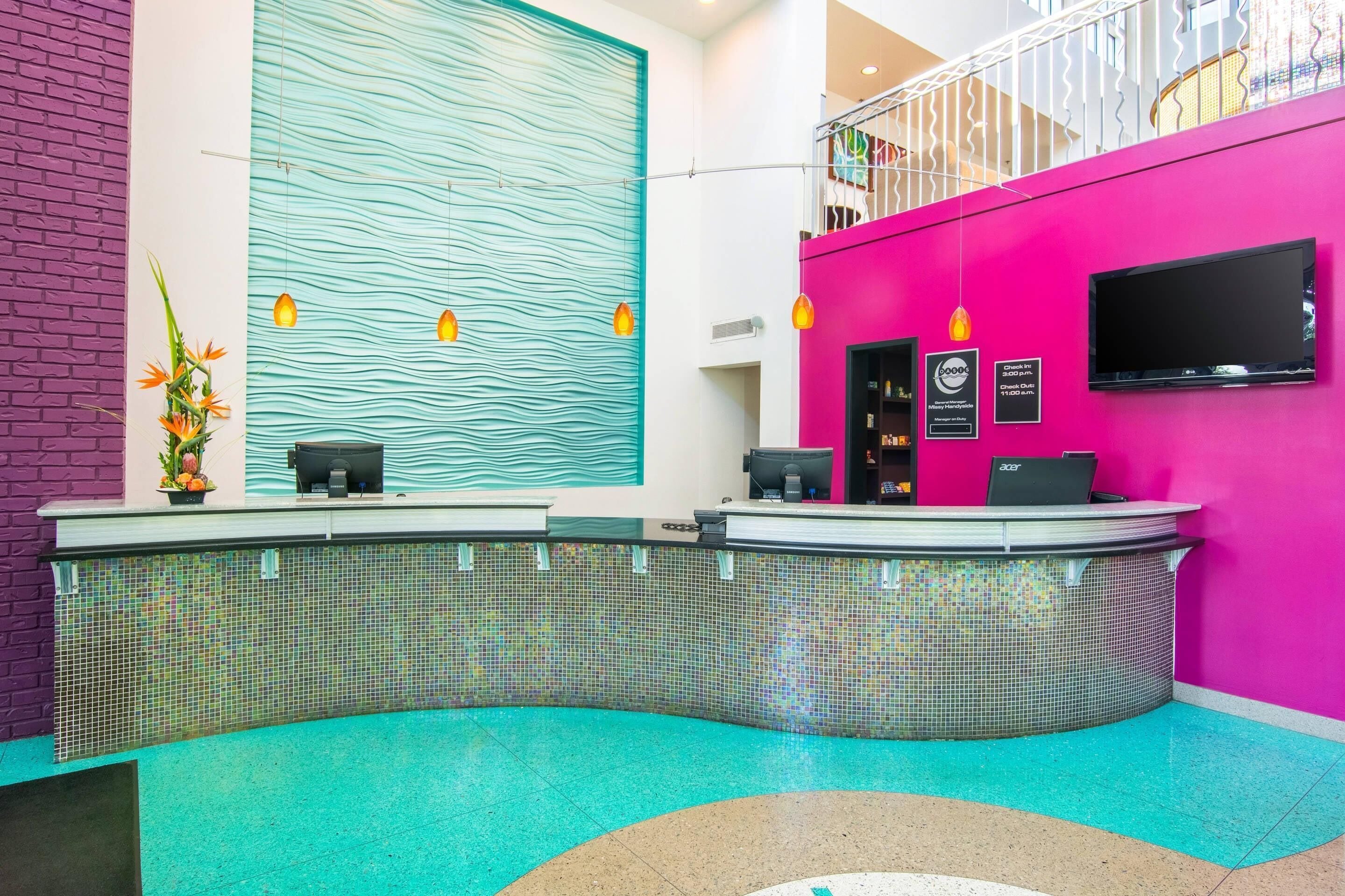 A reception area with a curved counter, a large window with a wavy pattern, and a pink wall with a mounted television.