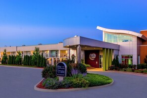 A hotel with a modern design, featuring a registration center sign, a curved entrance, and a landscaped area with shrubs and a small tree.