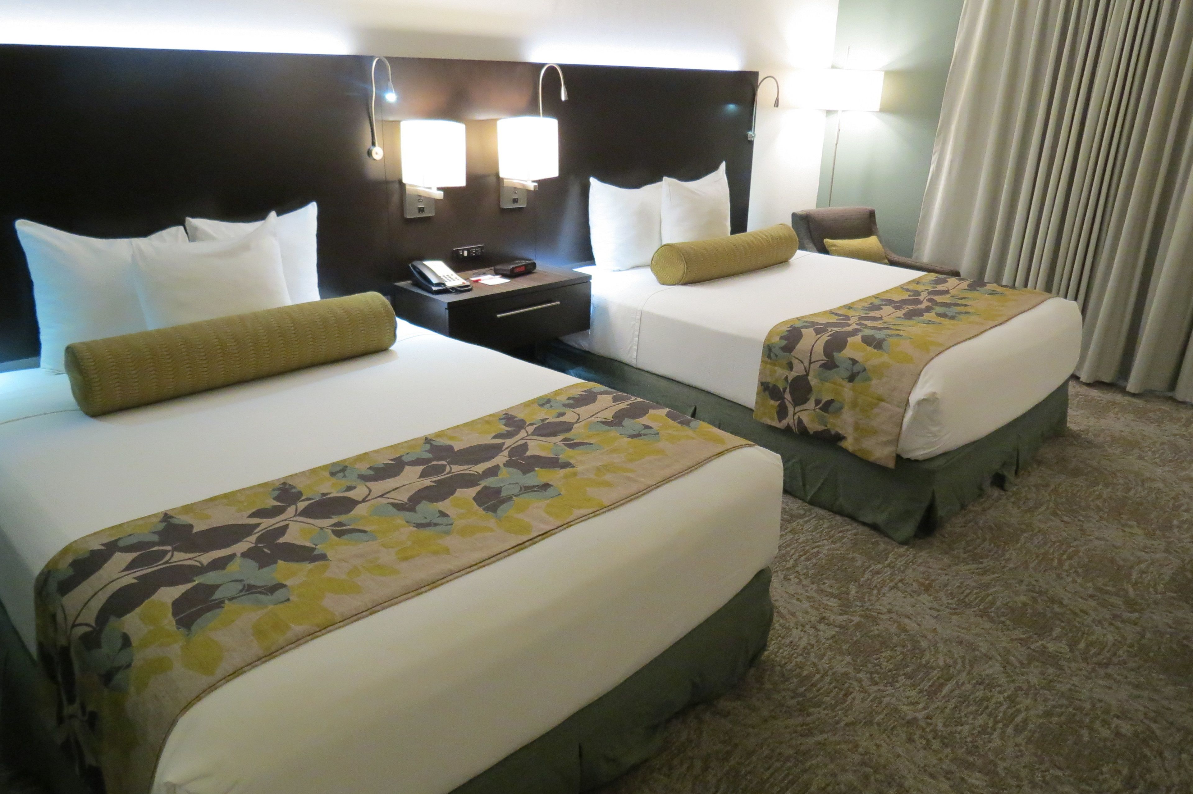 Habitación de hotel con dos camas, cada una con cubrecama floral, una mesita de noche con teléfono y una lámpara.