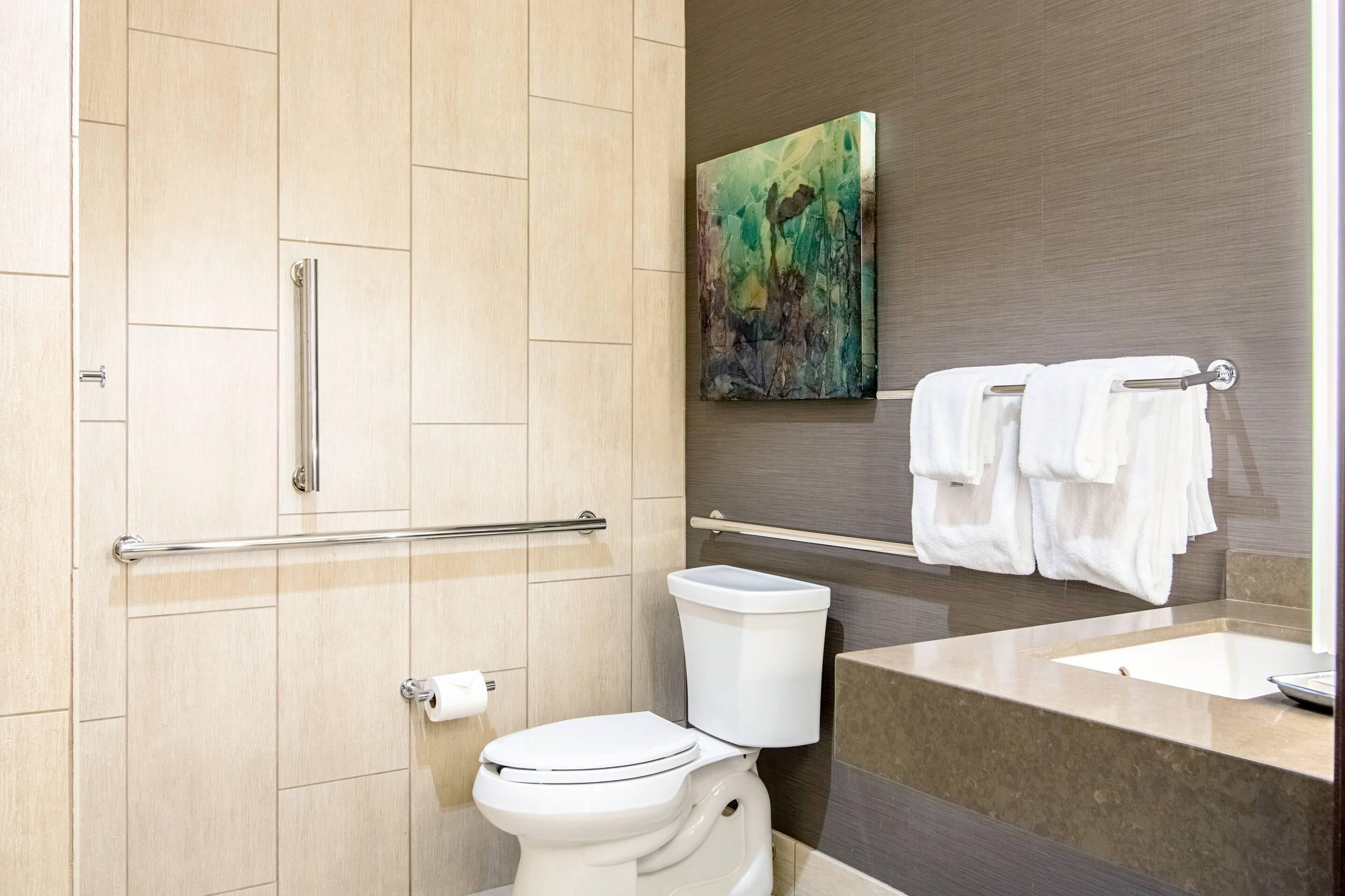Une salle de bain moderne équipée de toilettes, d’une barre d’appui, d’un porte-serviettes et d’un lavabo.