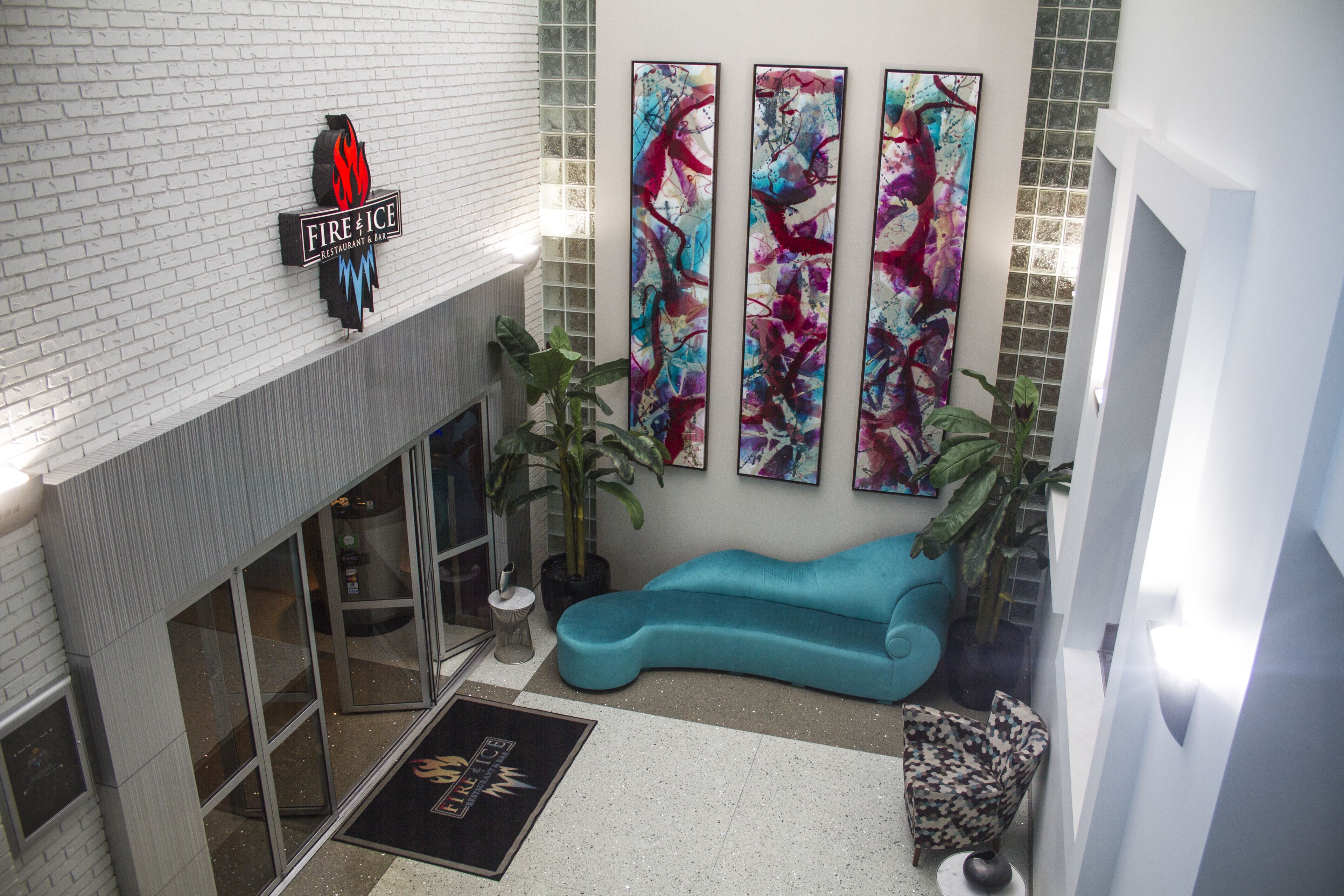 A modern lobby with a fire and ice restaurant sign, abstract art on the wall, a blue sofa, and potted plants.