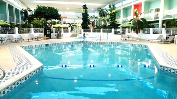 An indoor swimming pool with clear water, surrounded by lounge chairs and umbrellas.