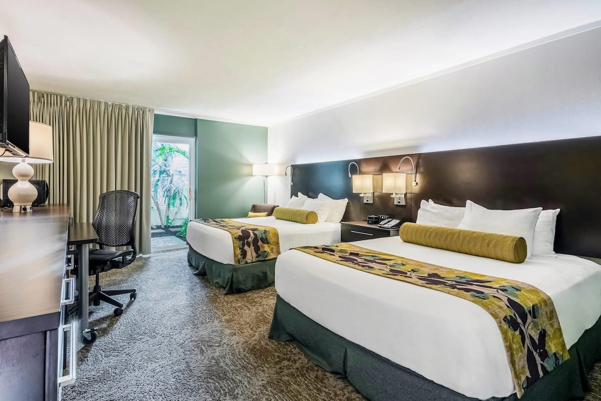 Una habitación de hotel con dos camas, un escritorio con silla, televisor y ventana con cortinas.