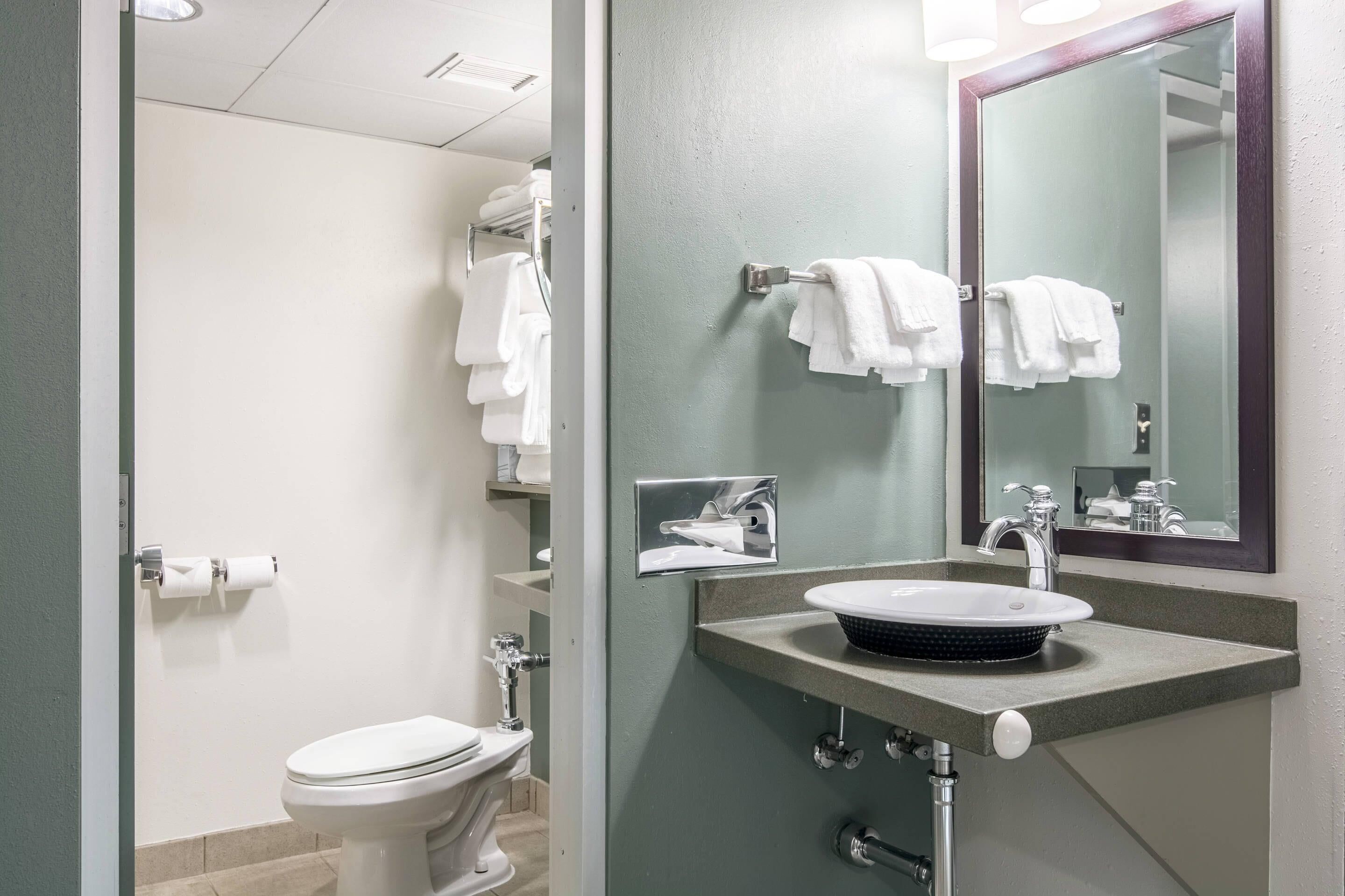 A bathroom with a white toilet, a sink with a mirror above it, and a towel rack with white towels.