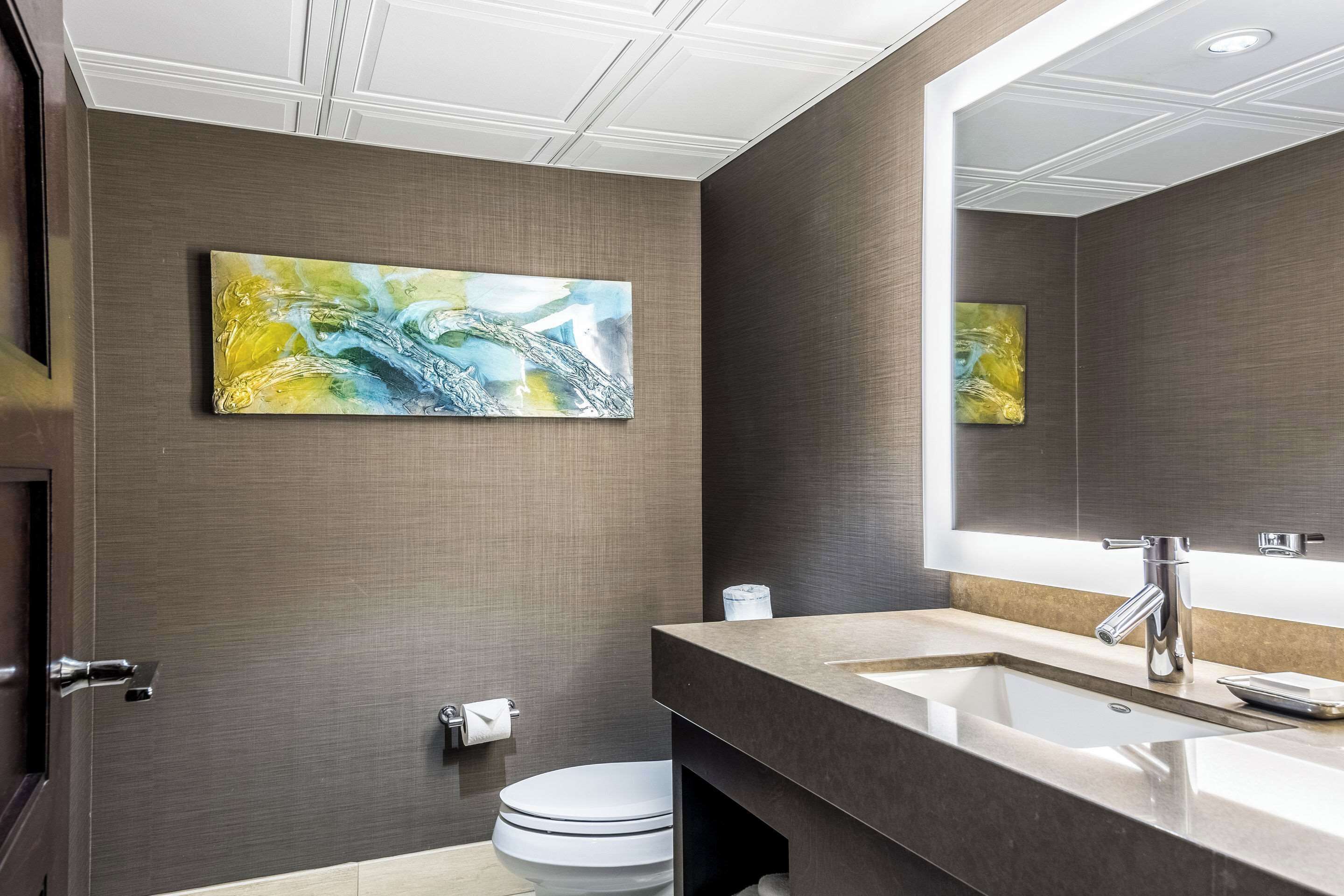 A modern bathroom with a large mirror, a sink, and a toilet.