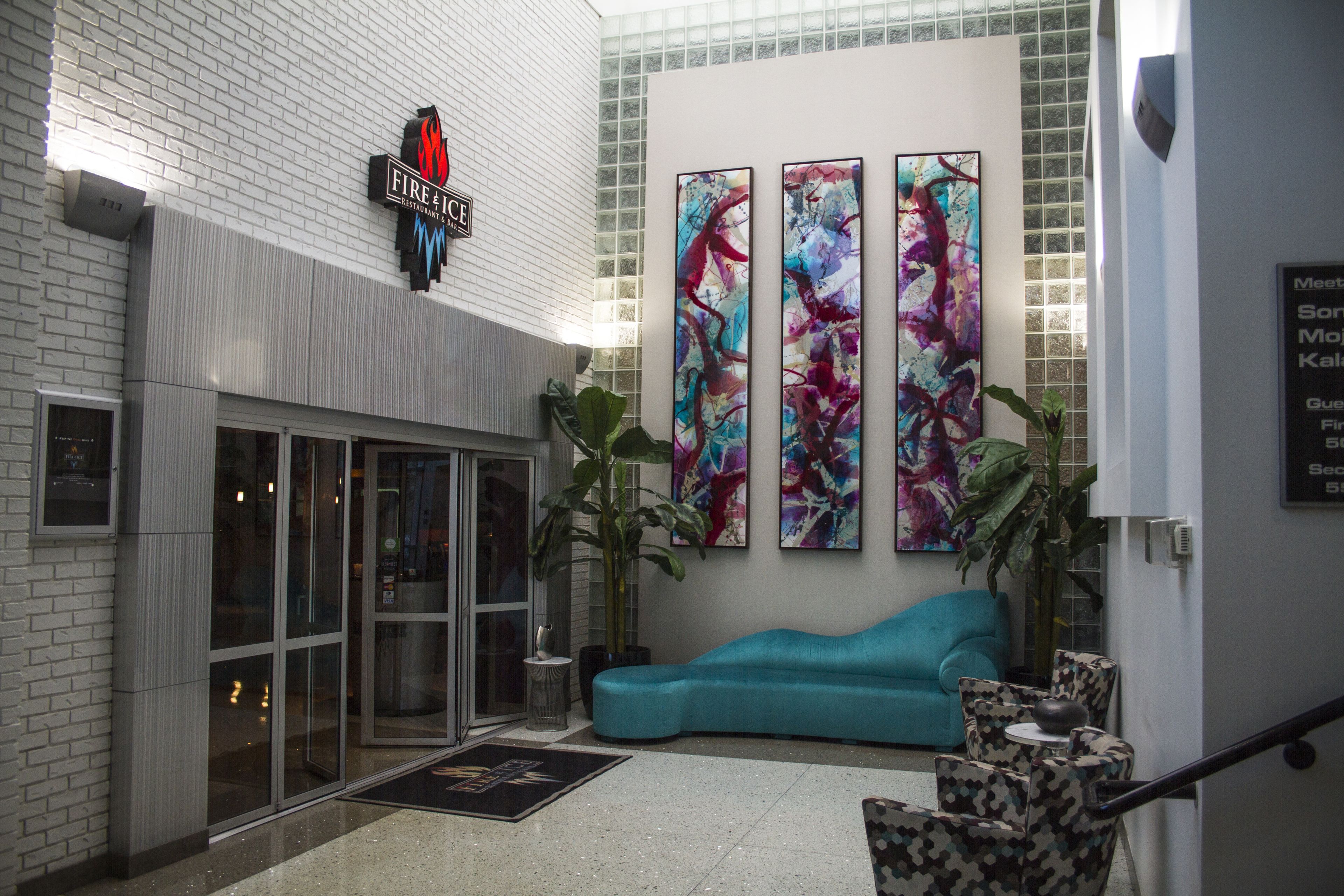 A hotel lobby with a glass entrance, a teal sofa, patterned chairs, and abstract art on the wall.