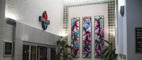 A hotel lobby with a glass entrance, a teal sofa, patterned chairs, and abstract art on the wall.