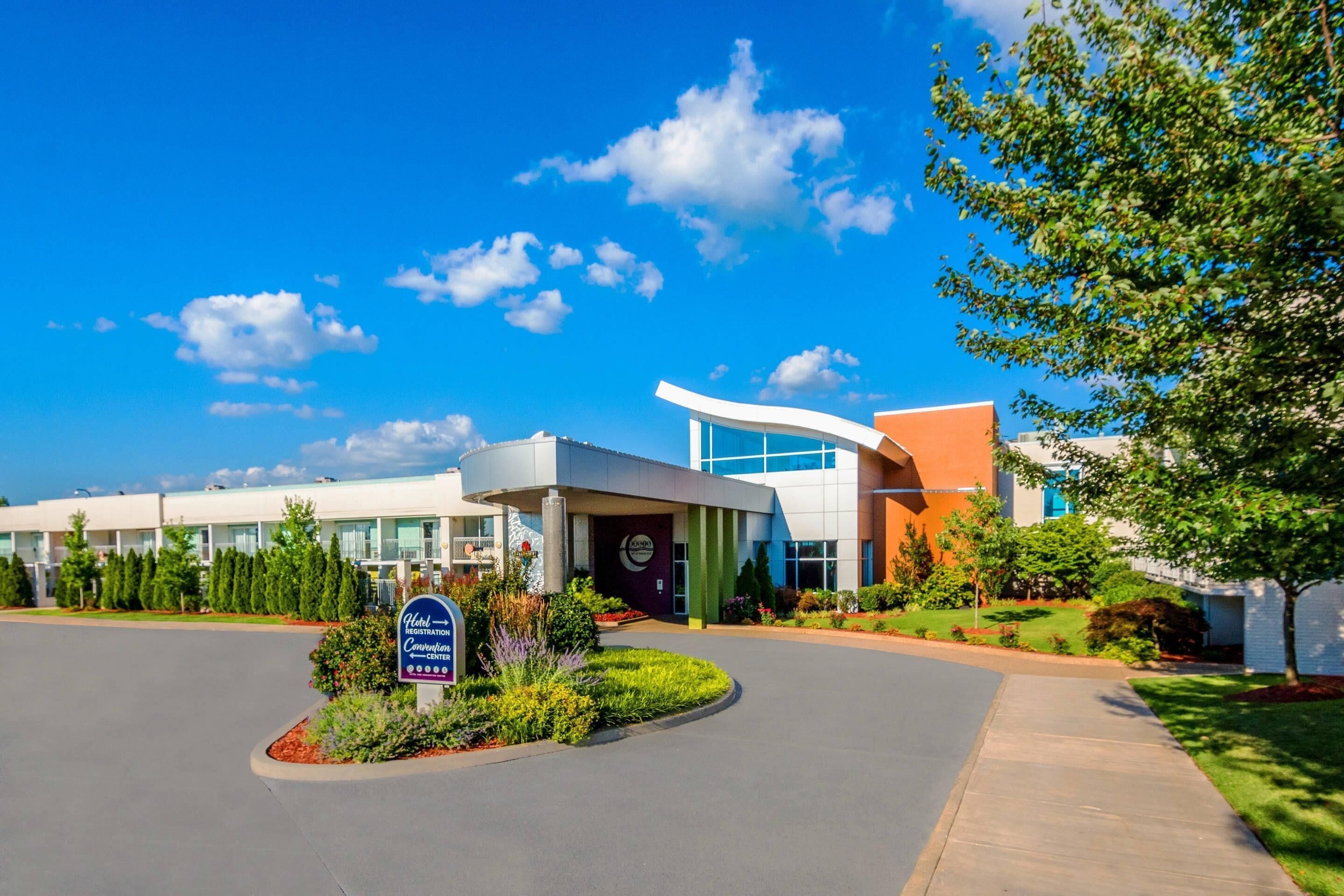 A modern hotel with a curved entrance, a landscaped garden, and a clear blue sky.