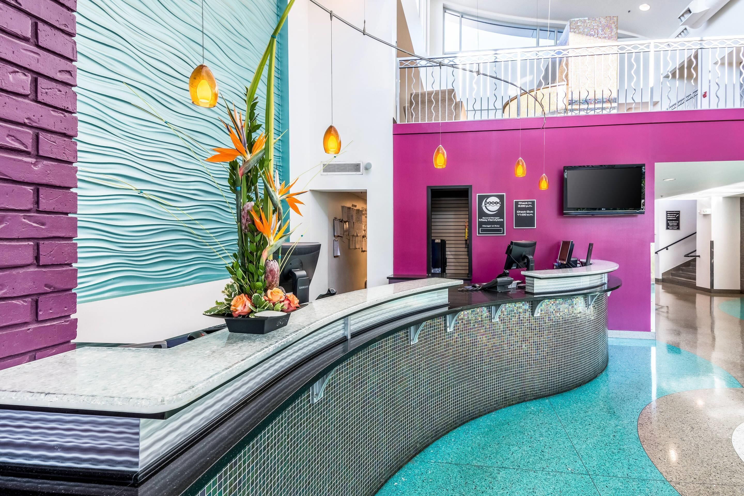 Zona de recepción con una barra curva, una planta con flores naranjas, un dispositivo Samsung y una pared rosa.