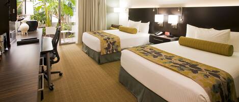 A hotel room with two beds, a desk, a chair, and a view of the outdoors.