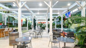 An outdoor patio area with tables and chairs, surrounded by greenery and a glass enclosure. - Oasis Hotel & Conv. Center, an Ascend Collection Hotel (Springfield)
