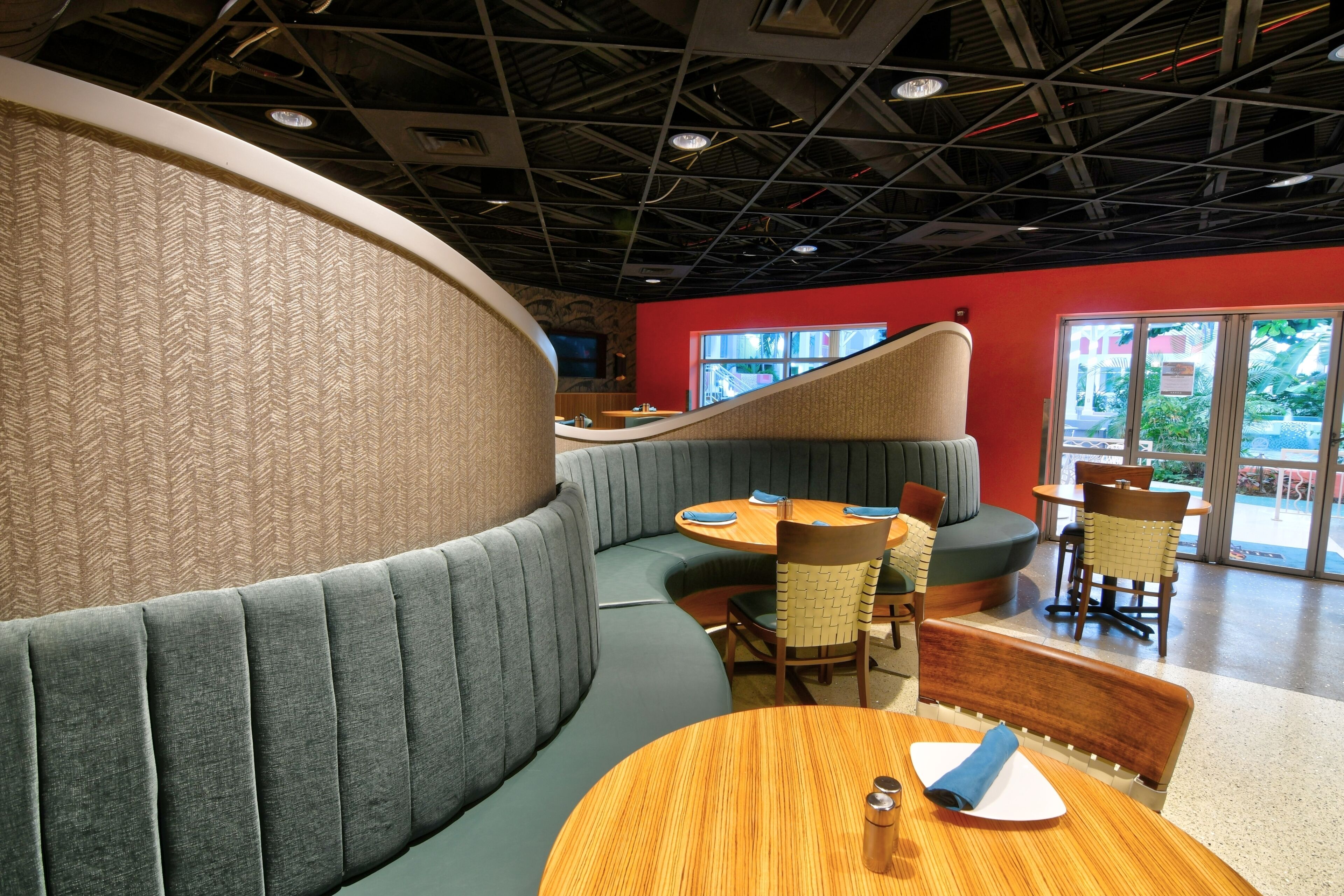 Un restaurante con una zona de asientos curvada, mesas de madera y una pared roja decorativa.
