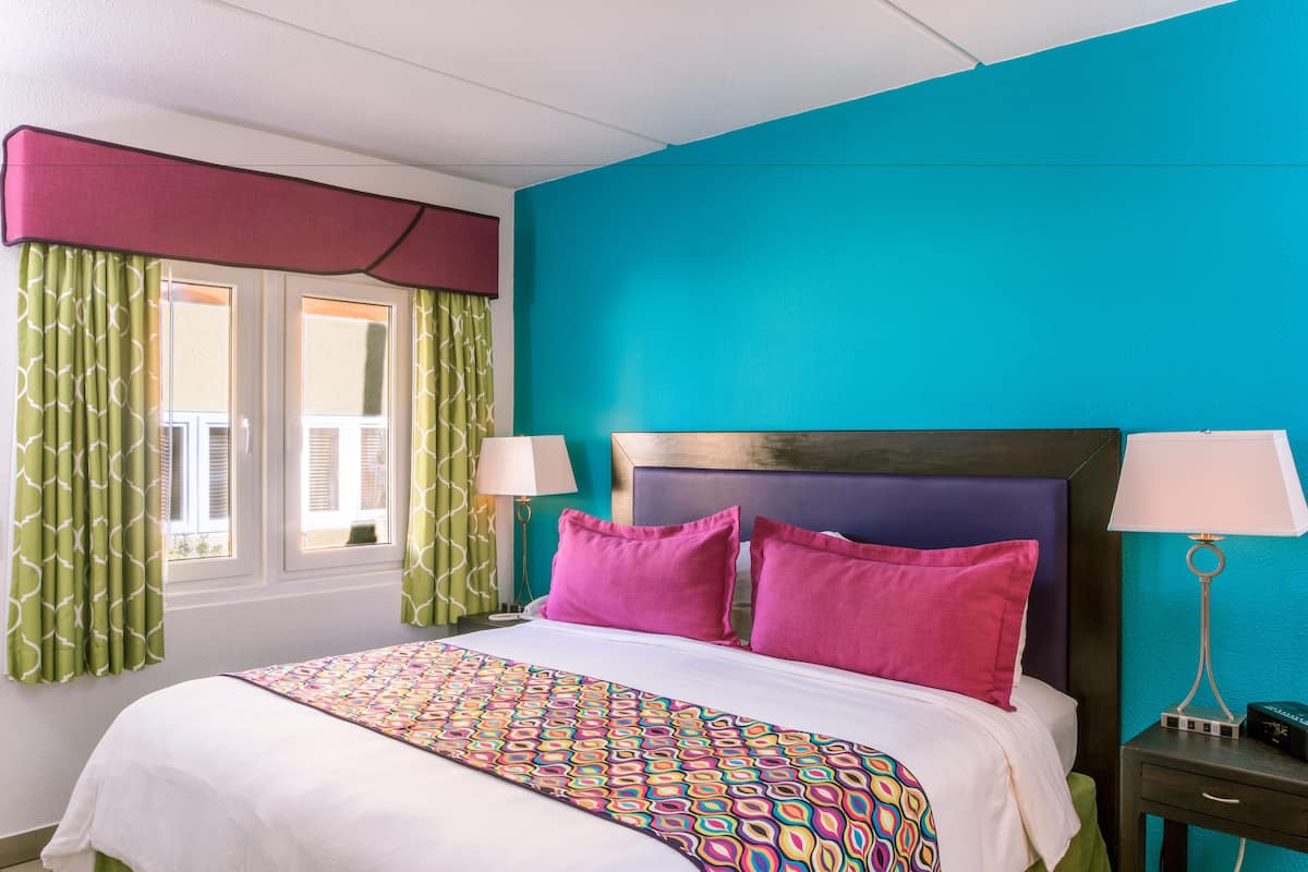 A hotel room with a bed, a nightstand, a lamp, and a window with curtains.