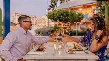 Una pareja brindando con copas de champán en una mesa al aire libre, con vistas a la ciudad de fondo.