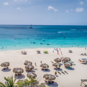 A beach with clear turquoise waters, a sandy shore, and several thatched umbrellas providing shade.