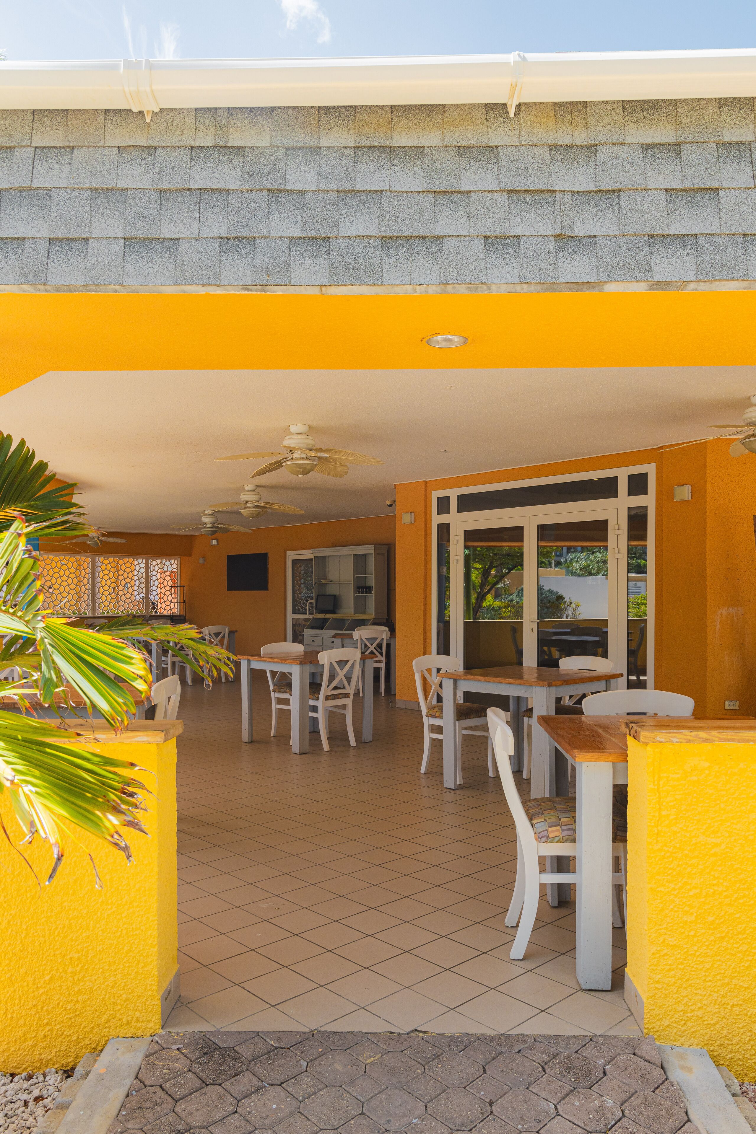 An outdoor dining area with a yellow wall, tiled floor, and white furniture.