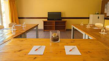 Une salle de conférence équipée de tables en bois, de chaises, d’un téléviseur et d’une petite plante décorative.