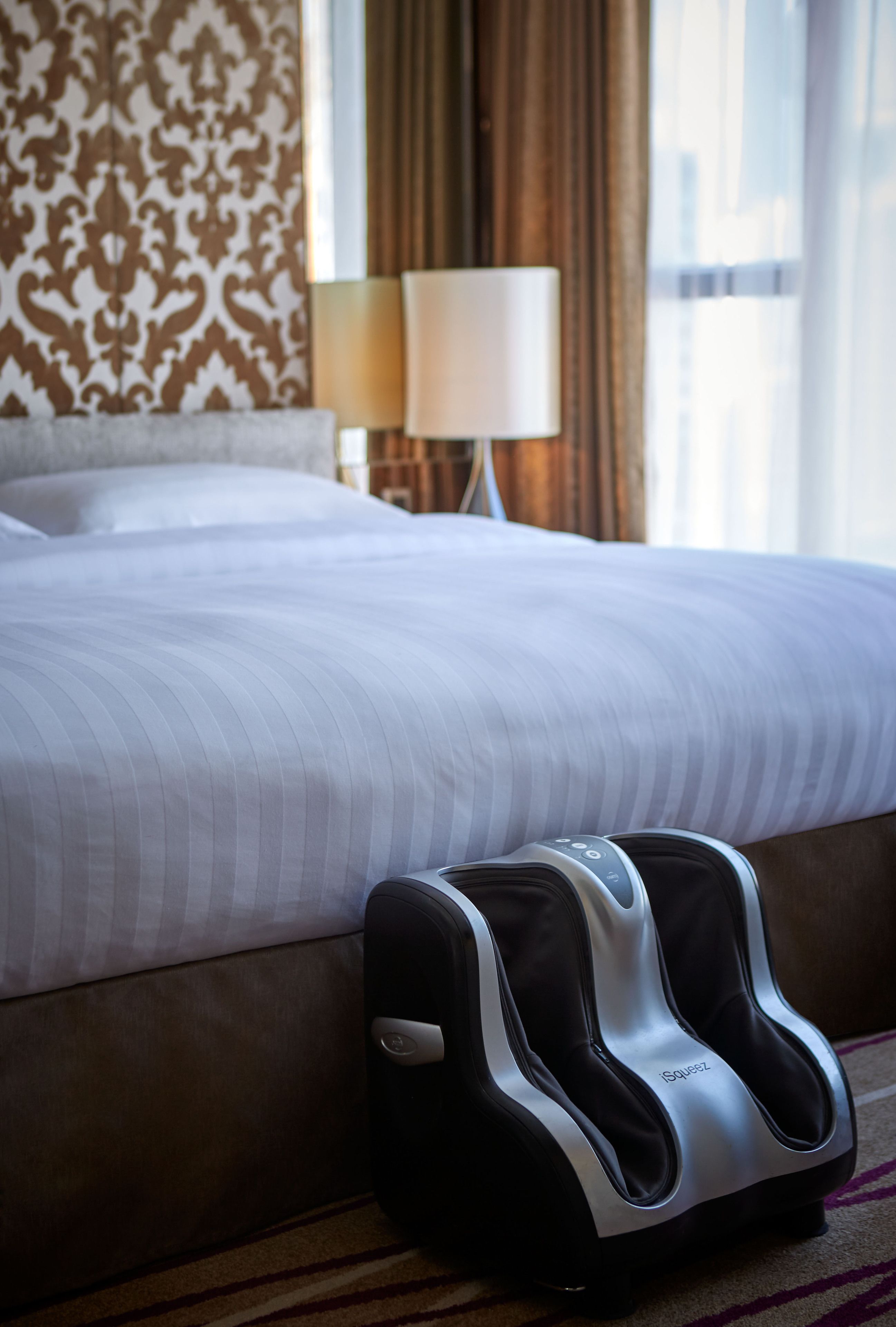 A hotel room with a bed, a massage chair, a lamp, and a window with curtains.