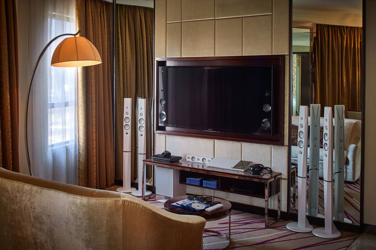 Habitación de hotel con una televisión de pantalla plana grande, un sofá, una mesa de centro, una lámpara y un equipo de sonido.
