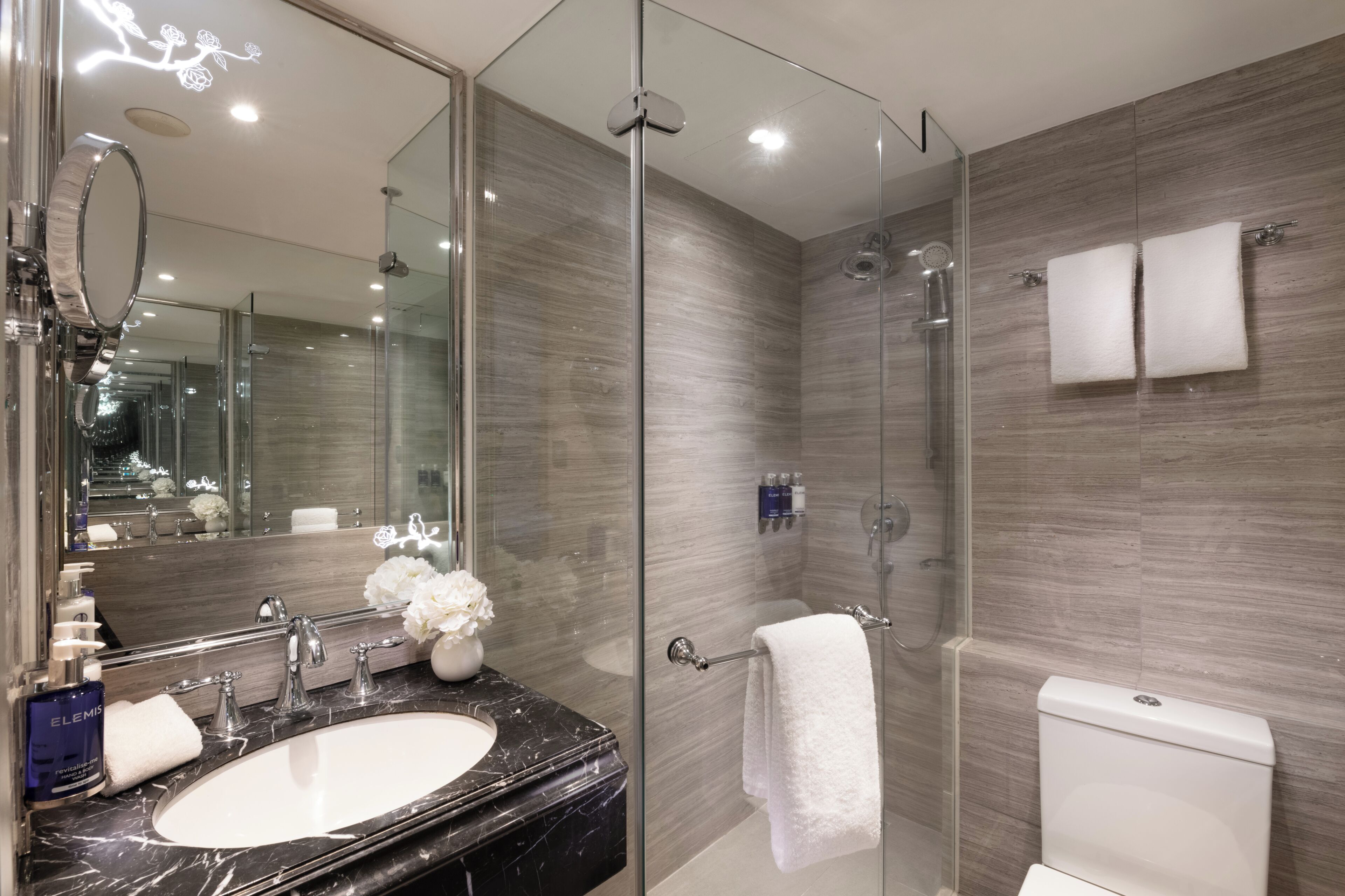 Un baño moderno con ducha de vidrio, lavamanos de mármol y un espejo grande.