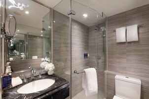Un baño moderno con ducha de vidrio, lavamanos de mármol y un espejo grande.
