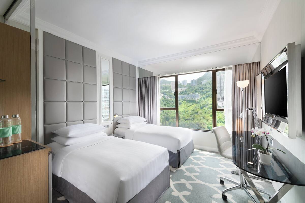 Habitación de hotel con dos camas, un escritorio, televisión y vistas a zonas verdes.