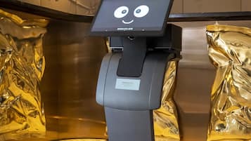 A self-service kiosk with a digital screen displaying a cartoon face, positioned in a lobby with marble flooring and decorative wall panels.