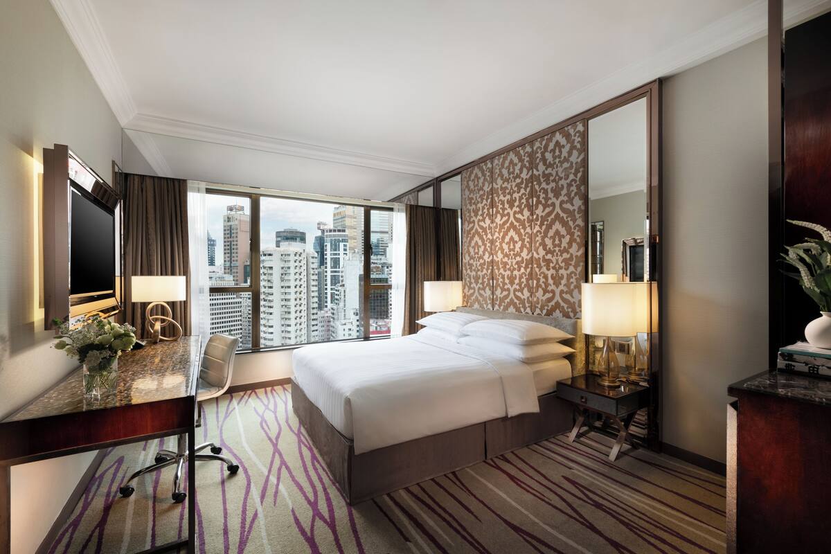 Habitación de hotel con una cama grande, un escritorio con silla, una lámpara de escritorio, un espejo y vistas a la ciudad.