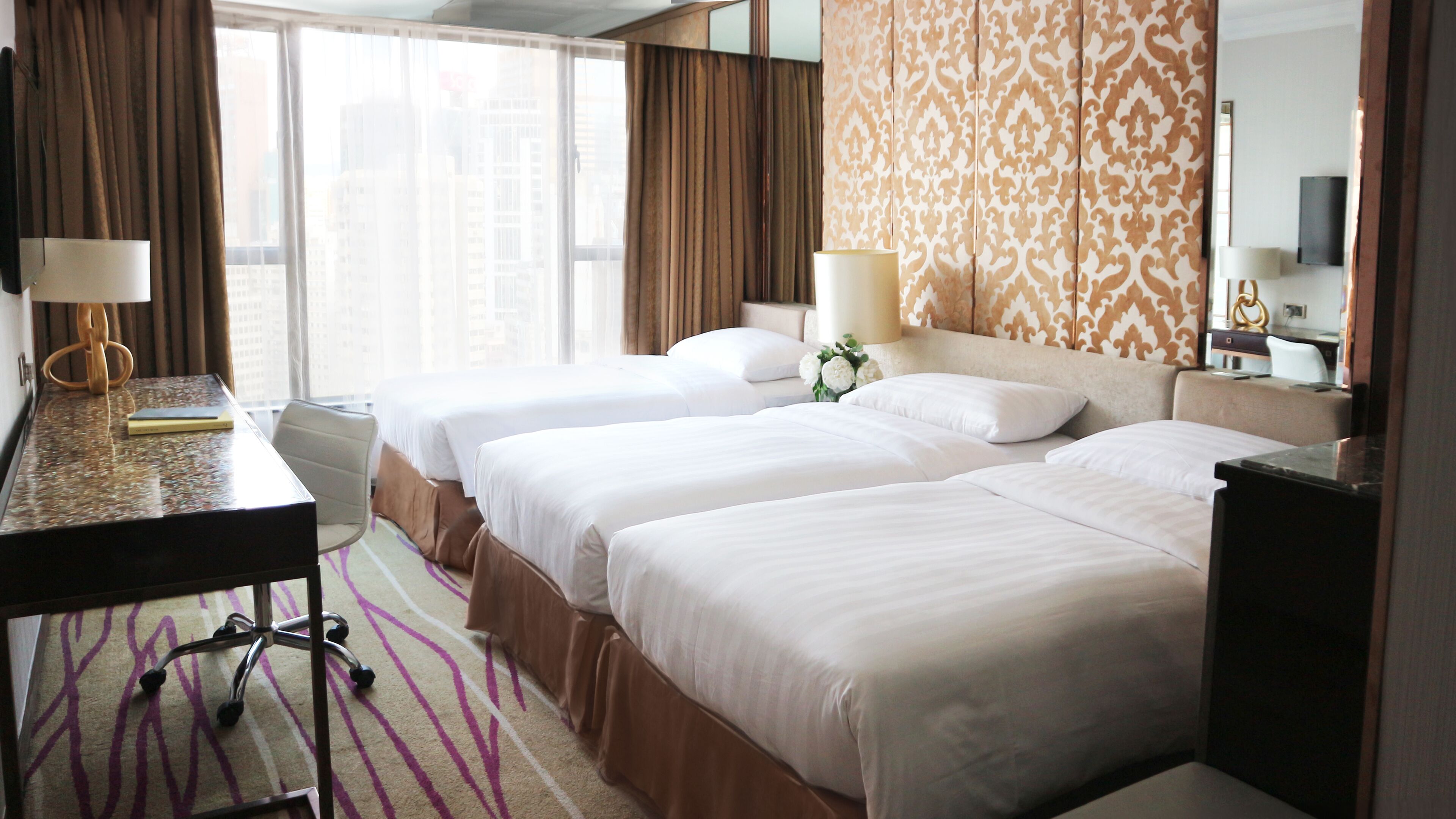 A hotel room with two beds, a desk, a chair, a lamp, and a large window with curtains.