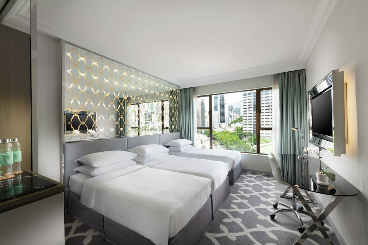 Habitación de hotel con dos camas, un escritorio, televisor y ventana grande con vista a la ciudad.