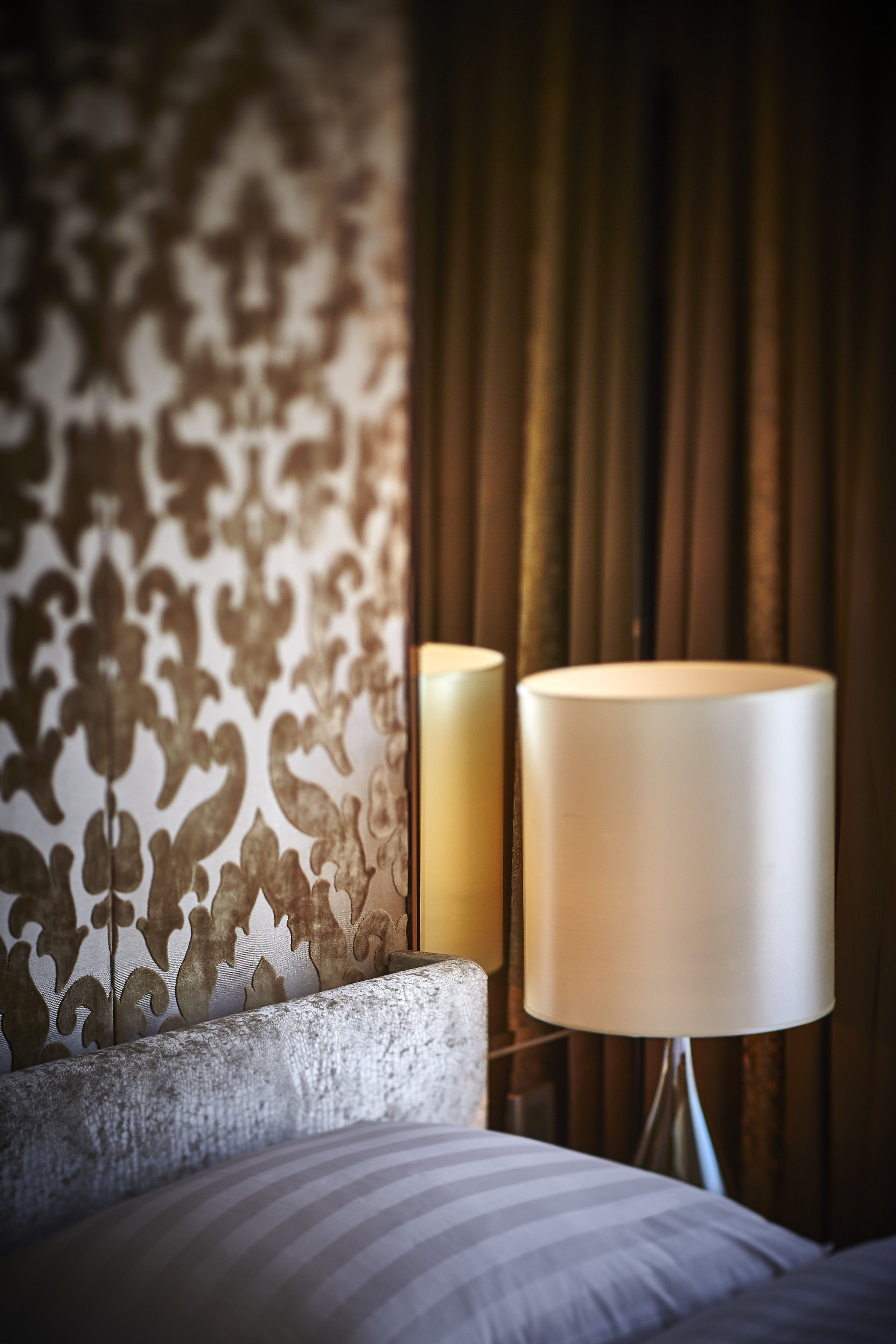 Un lit bien fait, avec un oreiller à rayures, une tête de lit texturée et un mur recouvert d’un papier peint à motifs.