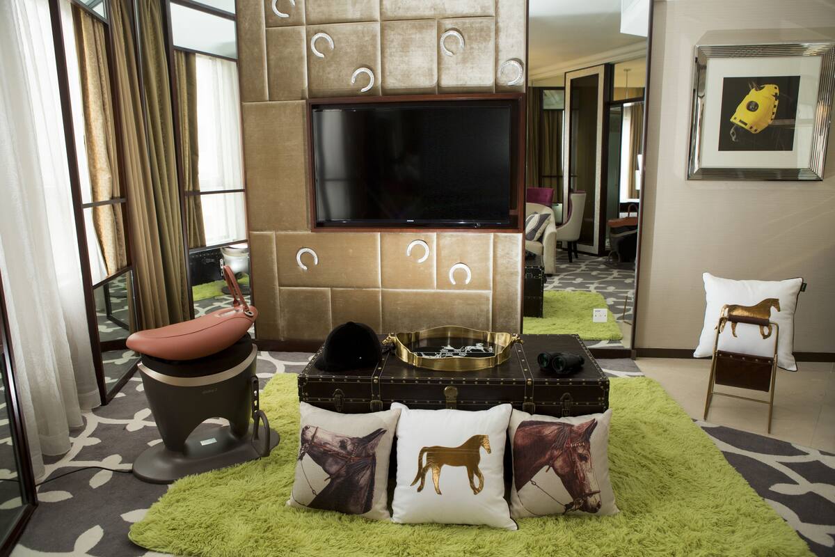 Una sala de estar moderna con un televisor de pantalla plana grande montado en la pared, un sofá de cuero, un felpudo verde y almohadones decorativos con motivos de caballos.