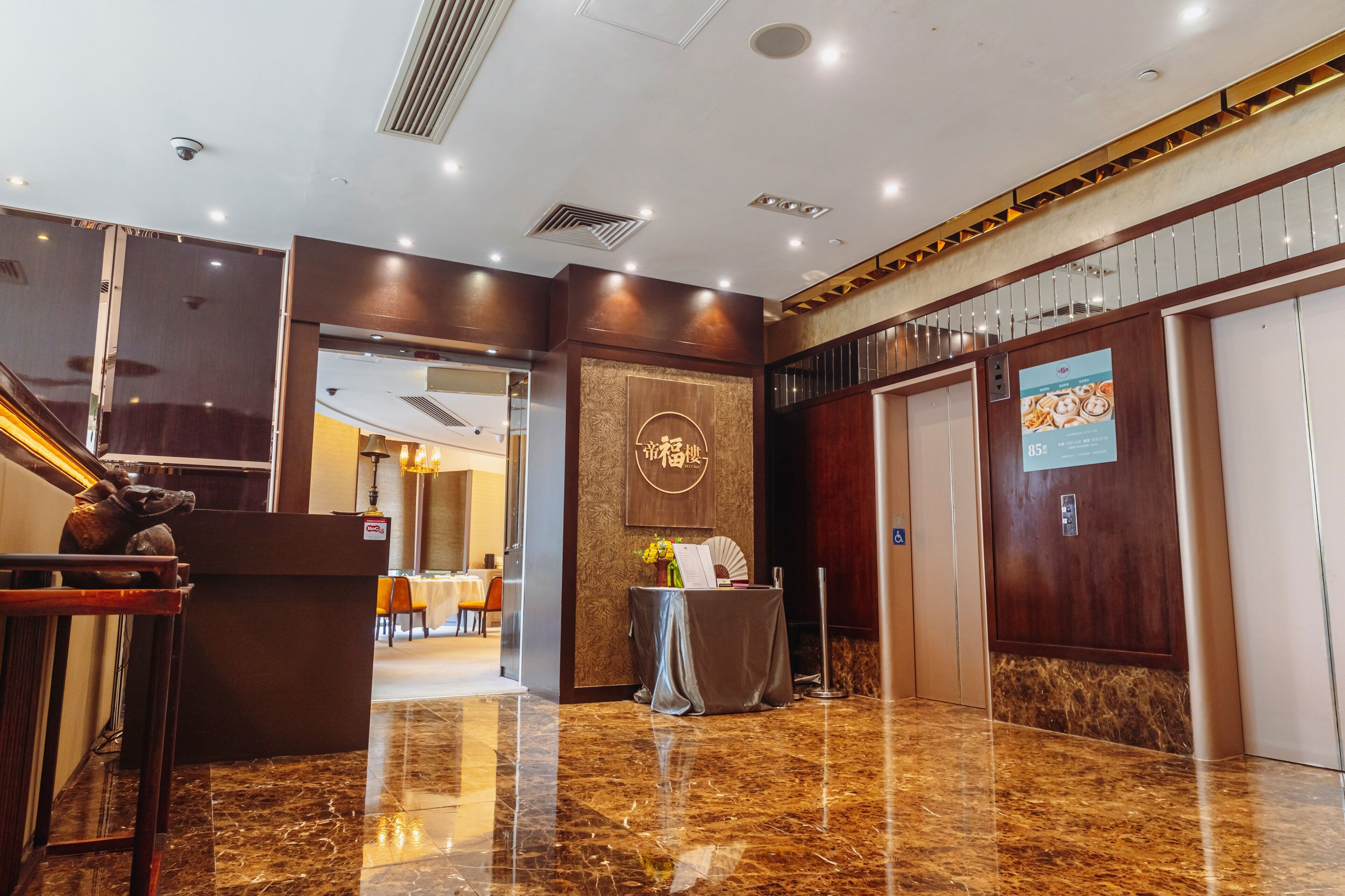 A hotel lobby with a marble floor, a reception desk, a staircase, and an elevator.