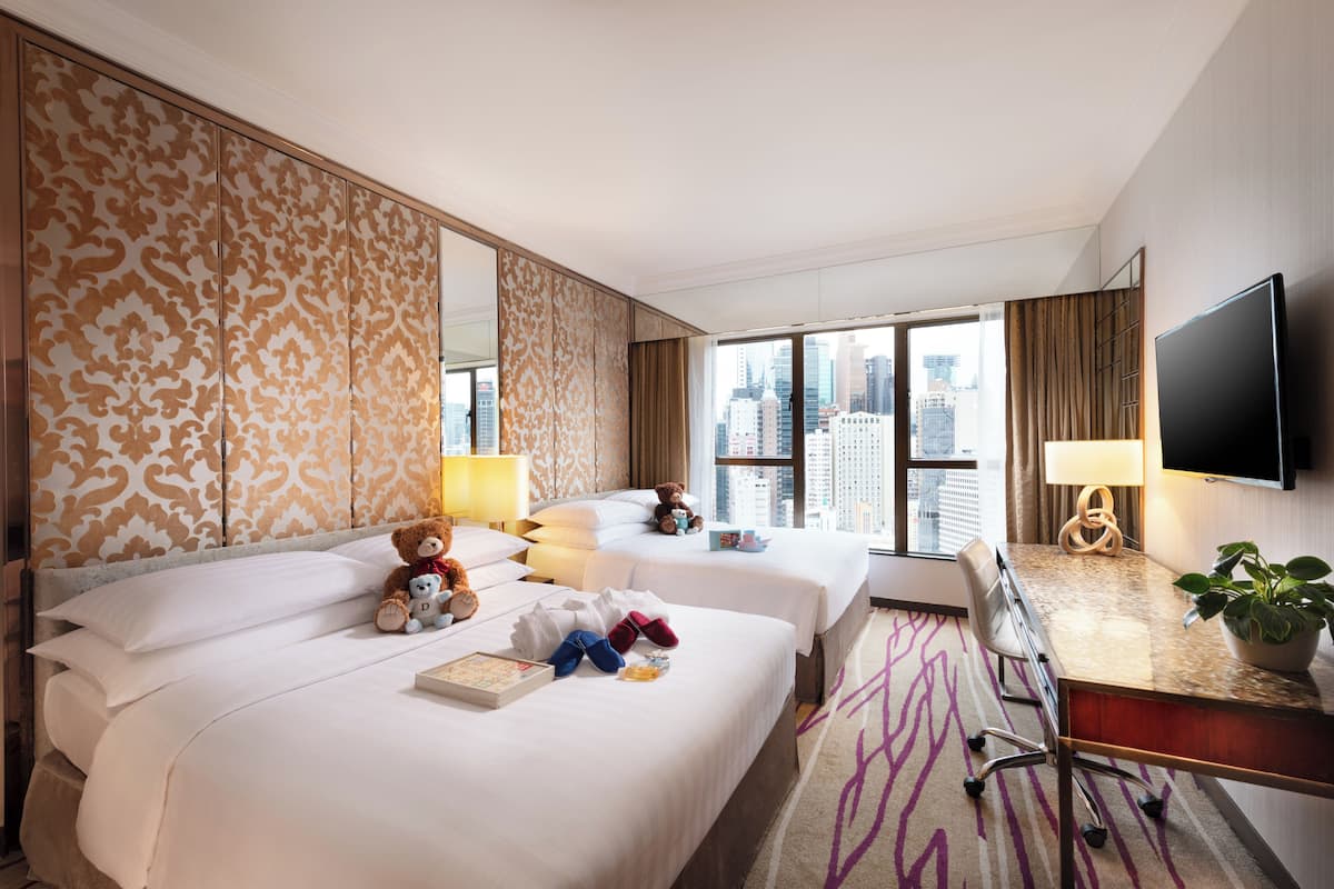 Habitación de hotel con dos camas, un escritorio, un televisor y vista a la ciudad.