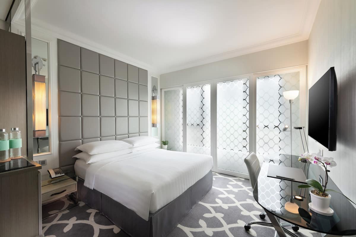 Una habitación de hotel moderna con una cama grande, un escritorio con silla, un televisor de pantalla plana y un ventanal con separador de vidrio.