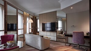 A modern hotel room with a large flat-screen TV, a sofa, a chair, a desk, and a mirror. - Dorsett Wanchai Hong Kong (Hong Kong)